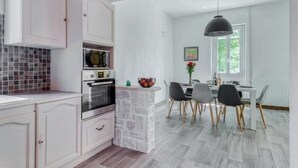 A modern kitchen with white cabinetry, a stone island, and a dining area with a table and chairs. - Ardeche in Provence with shady park (Pont-Saint-Esprit)