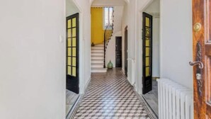 A hallway with checkered flooring leading to a staircase with a yellow wall and a green vase on the landing. - Ardeche in Provence with shady park (Pont-Saint-Esprit)