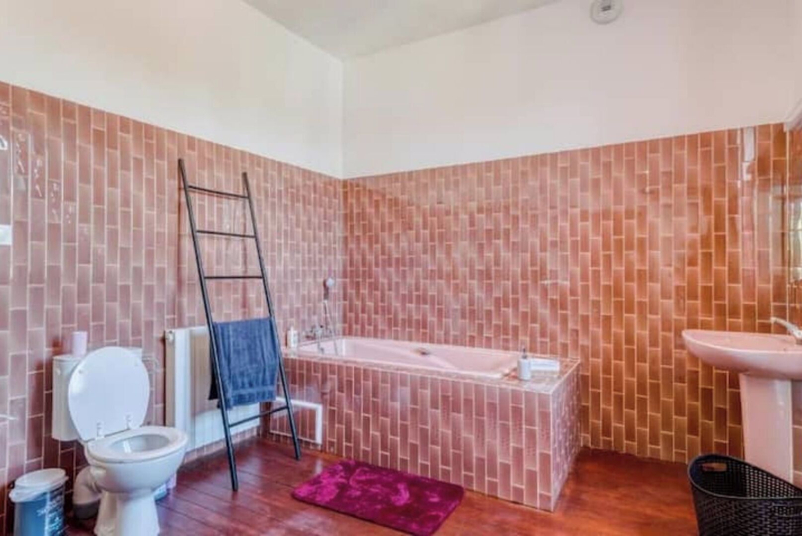 Een badkamer met bad, toilet en wastafel, met een wand betegeld in een baksteenmotief.