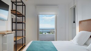 Ein Hotelzimmer mit Bett, Meerblick, einem Balkon und einem Schrank mit Regalen.