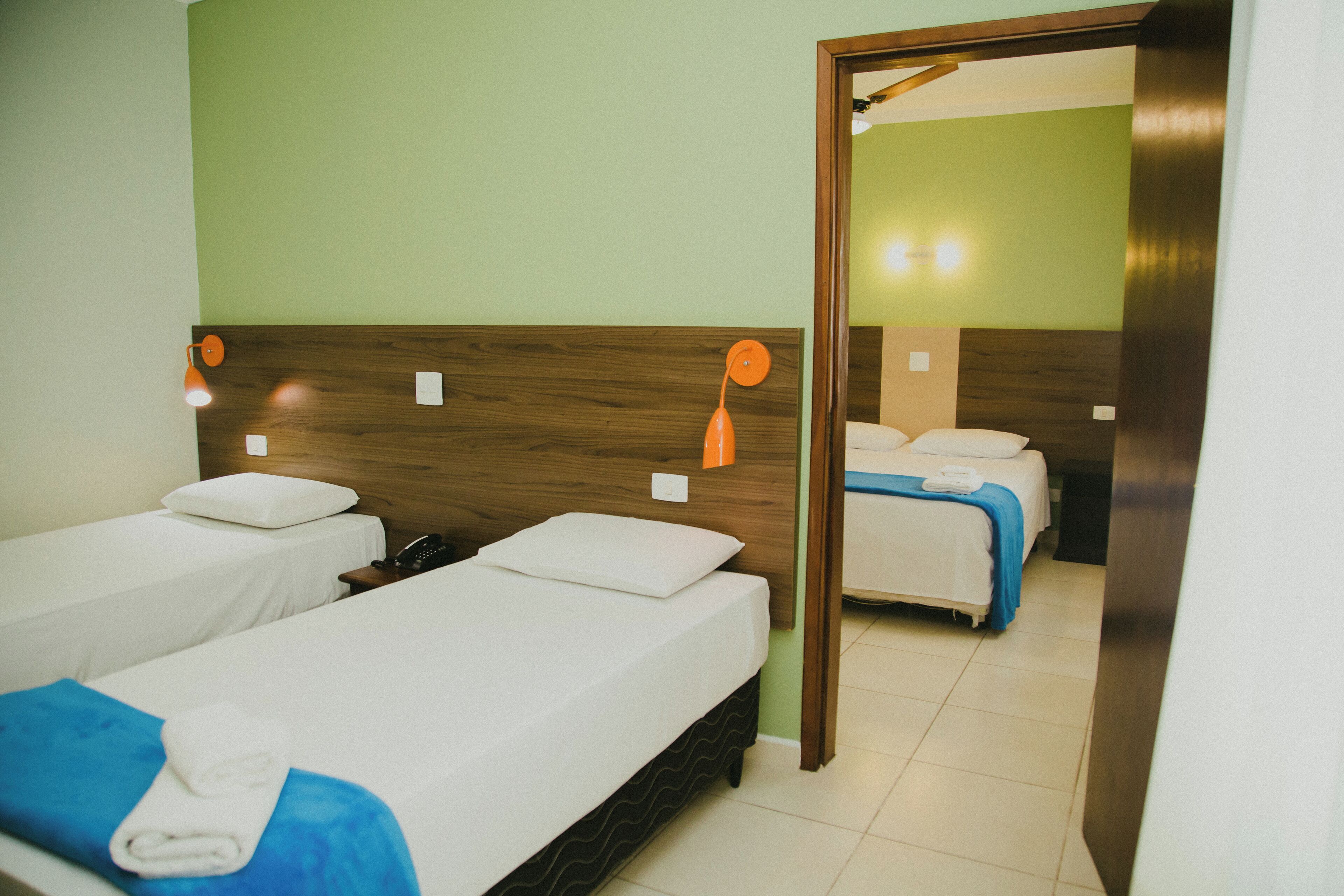 A hotel room with two single beds, a wooden headboard, a mirror, and a bathroom visible through an open door.