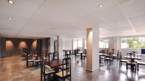 A spacious dining area with multiple tables and chairs, a tiled floor, and a high ceiling with recessed lighting. - Hotel Royal Park Piracicaba (Piracicaba)