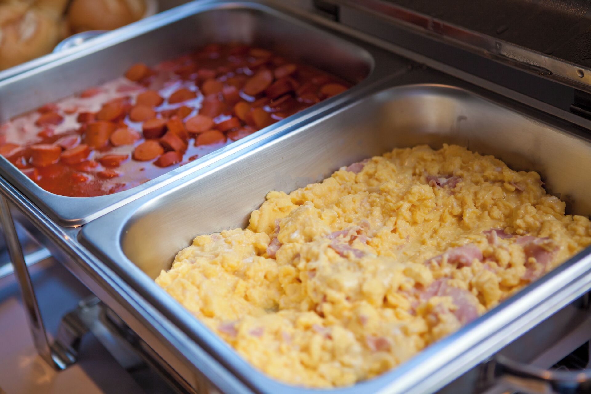 Un bufé con dos fuentes de comida: una con huevos revueltos y jamón, y otra con zanahorias en salsa roja.