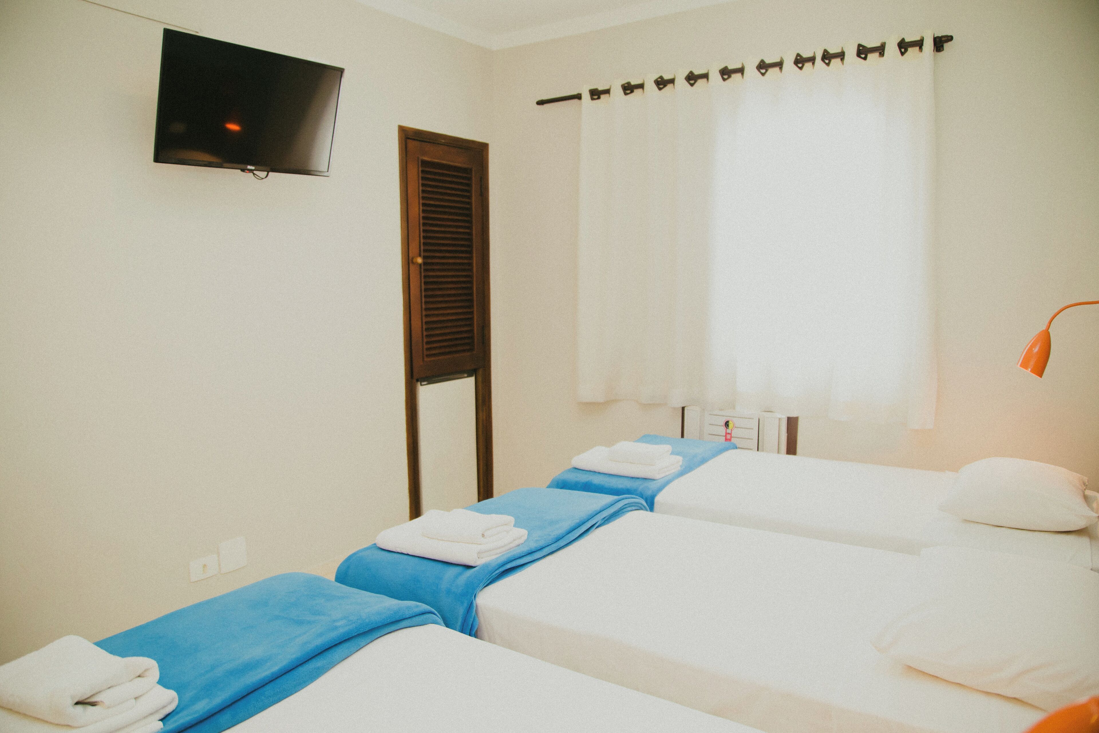 A hotel room with two beds, a TV mounted on the wall, a window with curtains, and a bedside lamp.