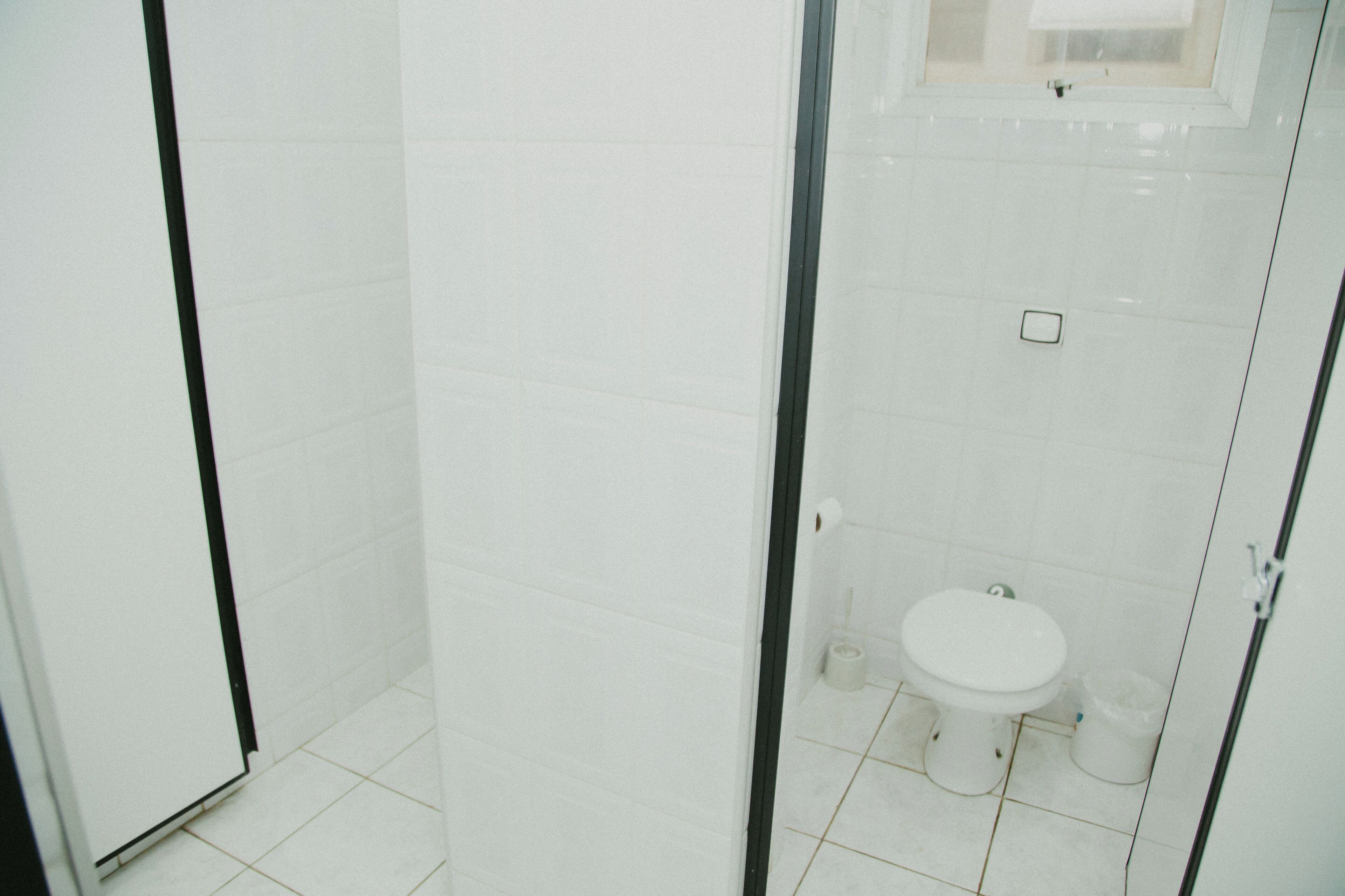 Un baño con azulejos blancos, inodoro y zona de ducha.