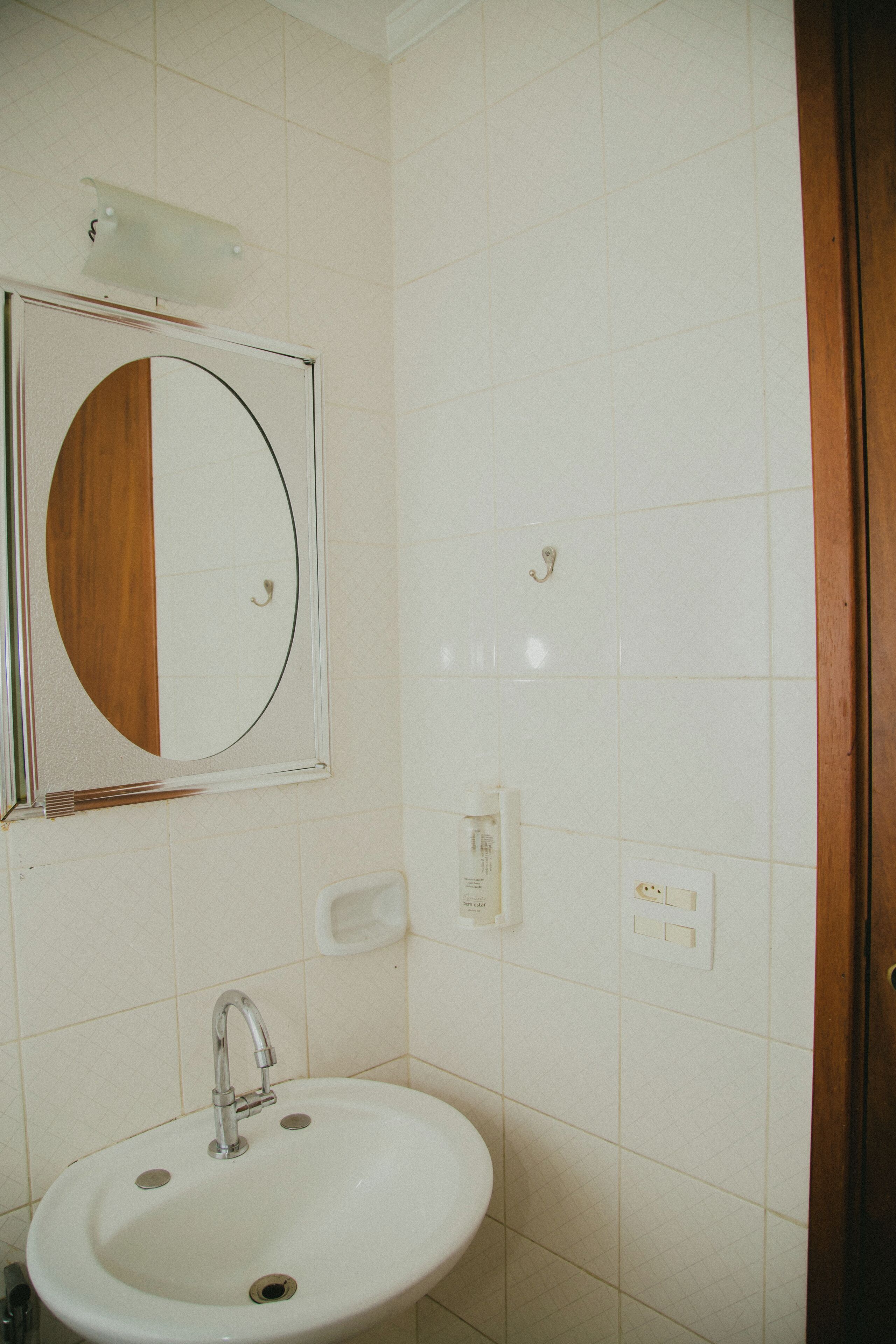 A bathroom with a white sink, a mirror with a wooden frame, and a light switch on the wall.