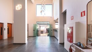 A spacious hallway with a glass door leading to an outdoor area, a fire extinguisher, and a fire alarm on the wall. - Hotel Royal Park Piracicaba (Piracicaba)