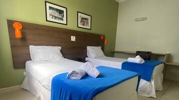 A hotel room with two beds, each with white linens and blue bedspreads. There are two framed pictures on the wall above the beds.