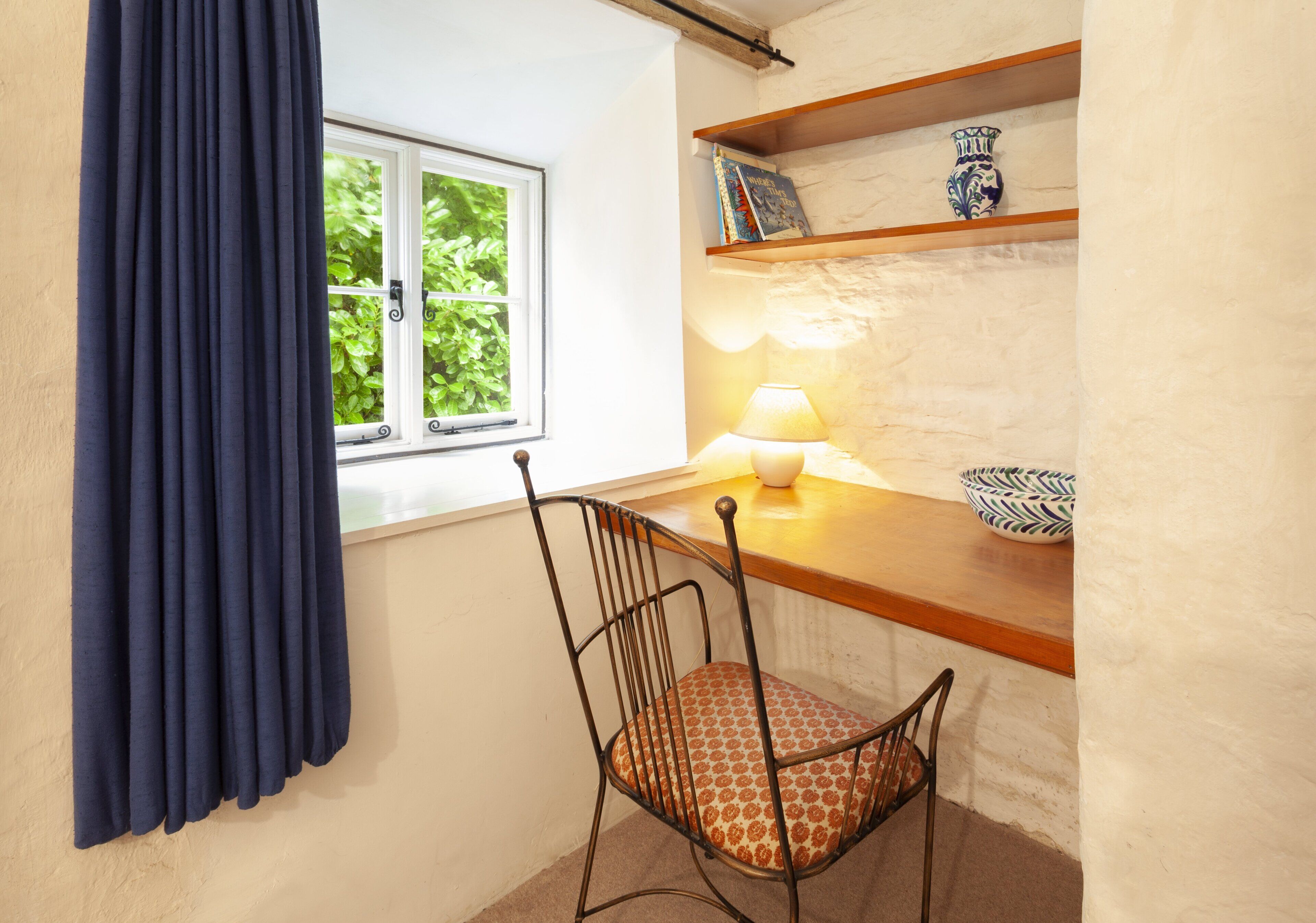 Une pièce avec une fenêtre, une chaise, une table avec une lampe et des étagères ornées d’objets décoratifs.