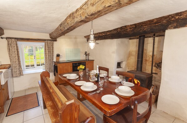 A dining area with a wooden table set for four, a bench, and a stone wall with a fireplace.