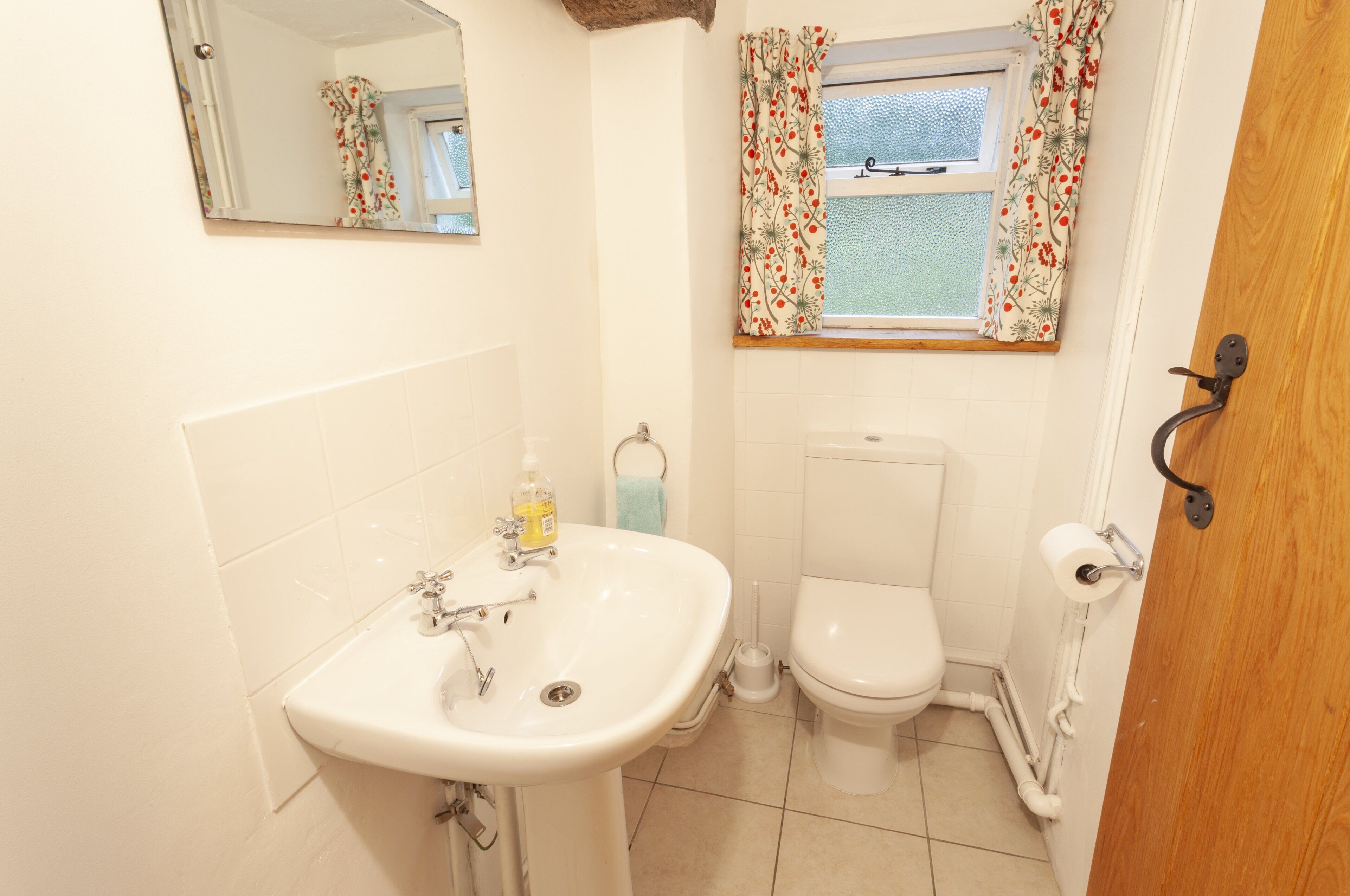 A bathroom with a sink, toilet, and window with floral curtains.