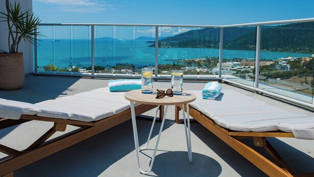 A balcony with two sun loungers, a small round table, and a potted plant. - Pacific Blue - Premiere (Airlie Beach)