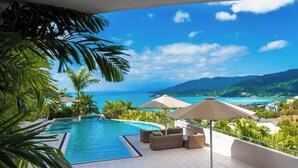 A pool area with a view of the sea and hills, furnished with chairs and umbrellas. - Pacific Blue - Premiere (Airlie Beach)