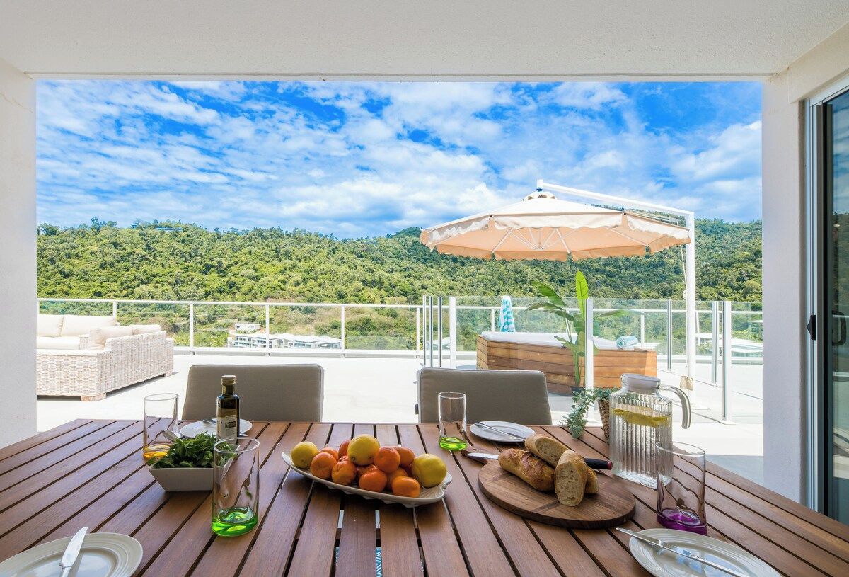 Un balcón con una mesa lista para comer, un sofá de mimbre y una sombrilla.
