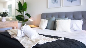 A neatly made bed with a black quilt, white pillows, and a white throw blanket.