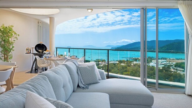 Una sala de estar moderna con un sofá grande, una zona de comedor con sillas y vistas al mar a través de ventanales amplios.