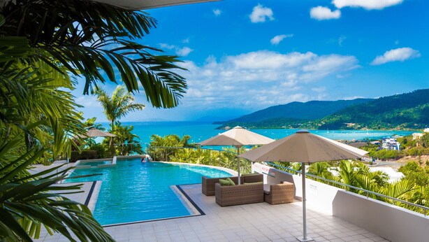A swimming pool with lounge chairs and umbrellas, overlooking a coastal view with mountains and greenery.