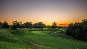 Ein Golfplatz mit gewundenem Weg, saftigem Grün und Bäumen unter einem Sonnenuntergangshimmel.