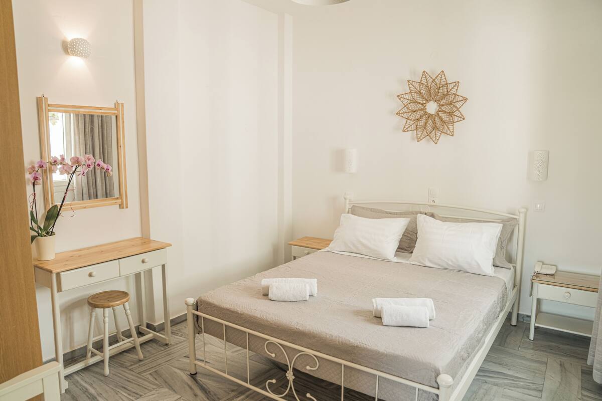 A bedroom with a bed, bedside tables, a desk with a chair, a mirror, and a wall decoration.