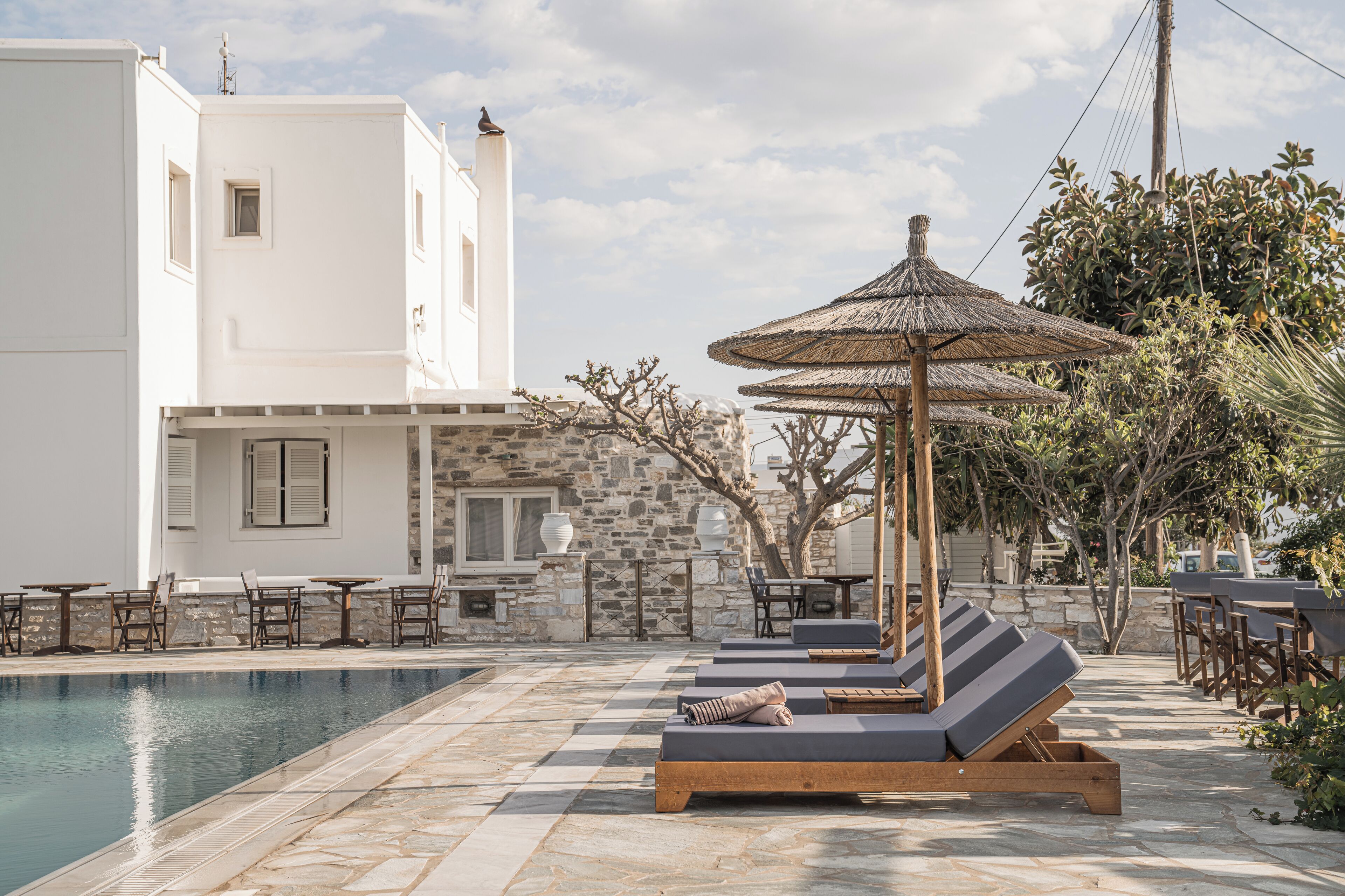 A poolside area with lounge chairs and umbrellas, a stone wall, and a white building with windows.