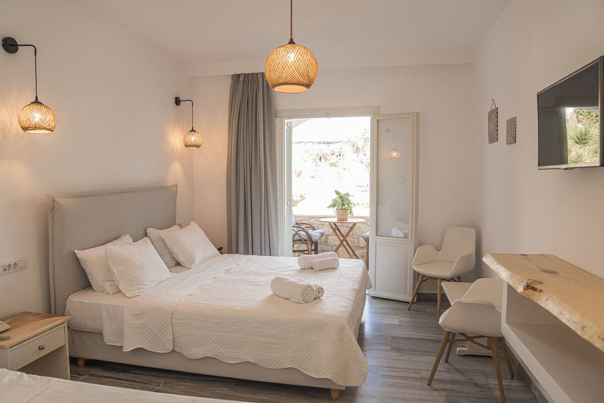 A bedroom with a large bed, bedside tables, a desk, and a chair. There is a window with a view of the outdoors.