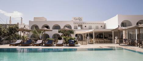 A pool area with lounge chairs and umbrellas, a sign for 'Christiana Hotel', and a building with arches and a white facade.