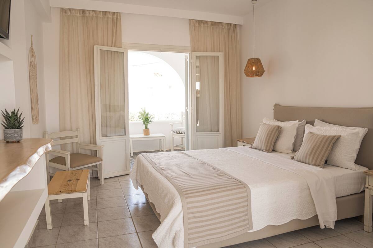 A bedroom with a large bed, a desk, a chair, and a small table with a plant.