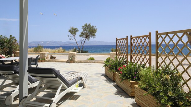 A terrace with lounge chairs, a table, and wooden planters with flowers. - Christiana Hotel (Paros)