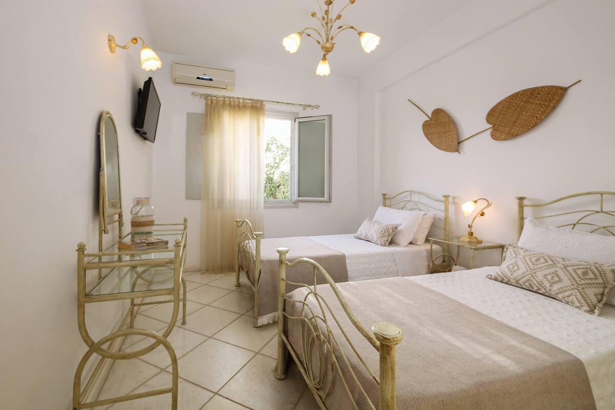 A bedroom with two beds, a mirror, a small table, and a window with curtains.