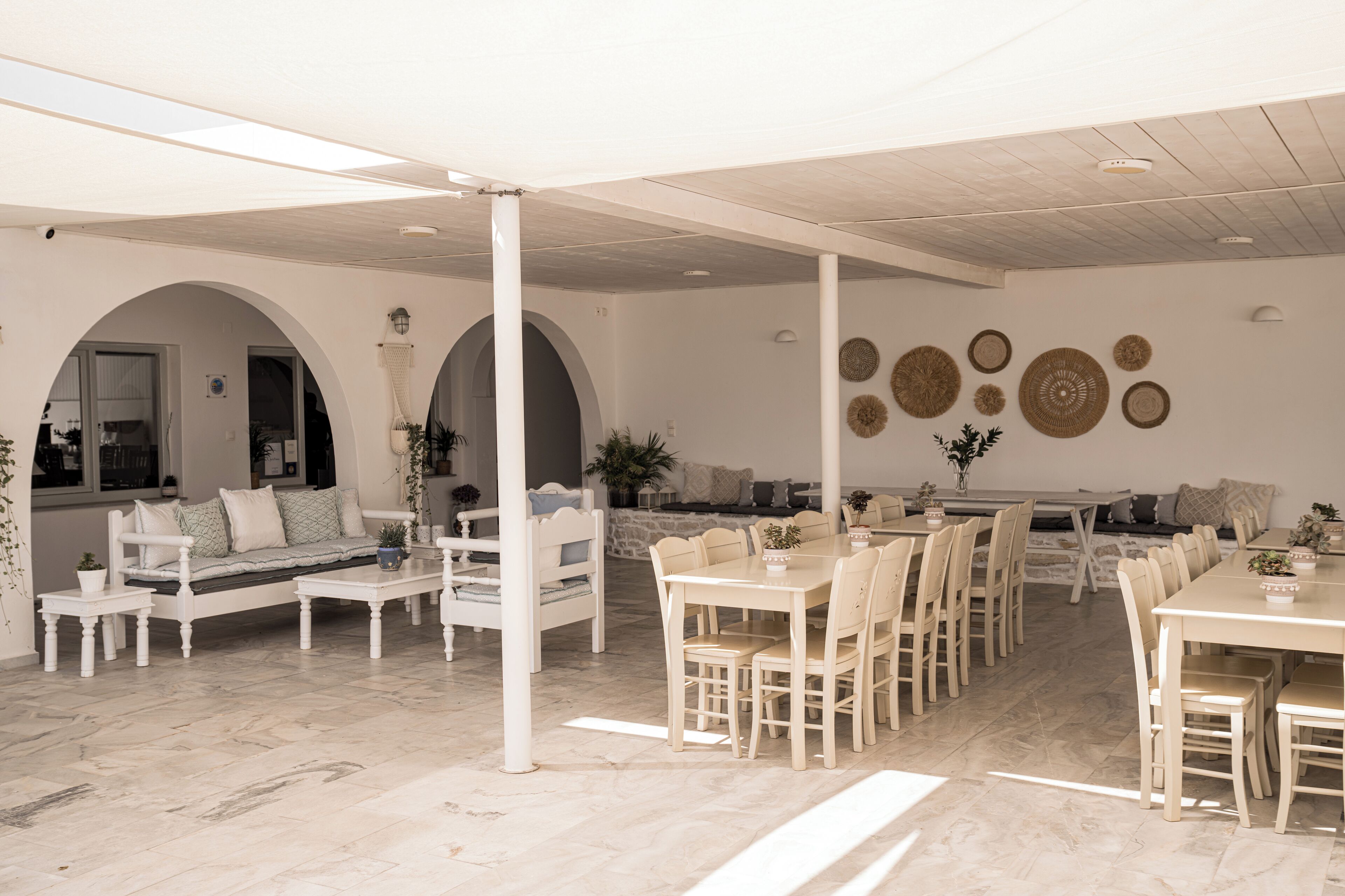 A spacious living area with a white sofa, dining table, and chairs. There are arches and a wall with decorative plates.