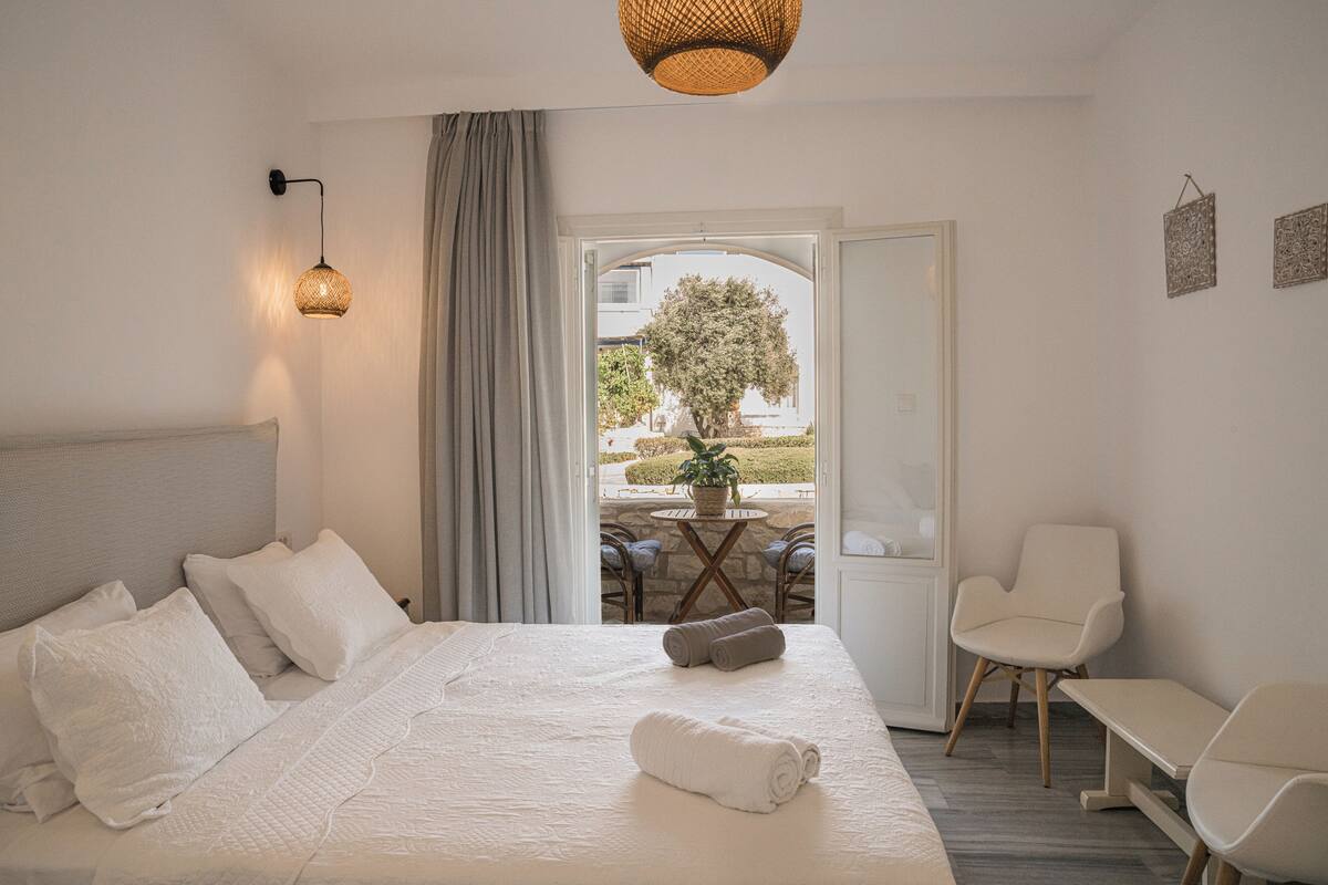 A hotel room with a bed, a chair, a table, and a view of the outside.