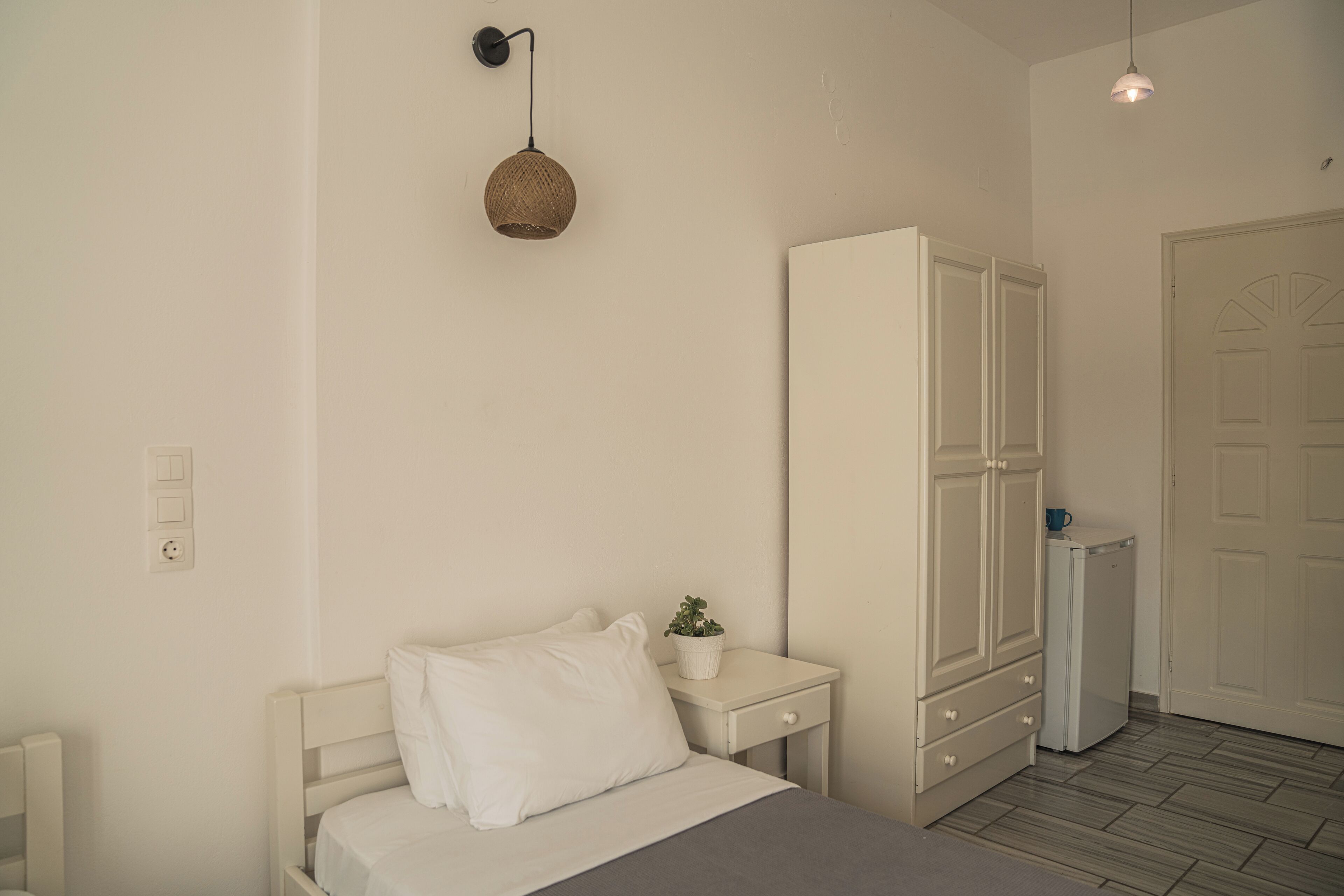 Un dormitorio con cama, mesita de noche, armario y una lámpara colgante.