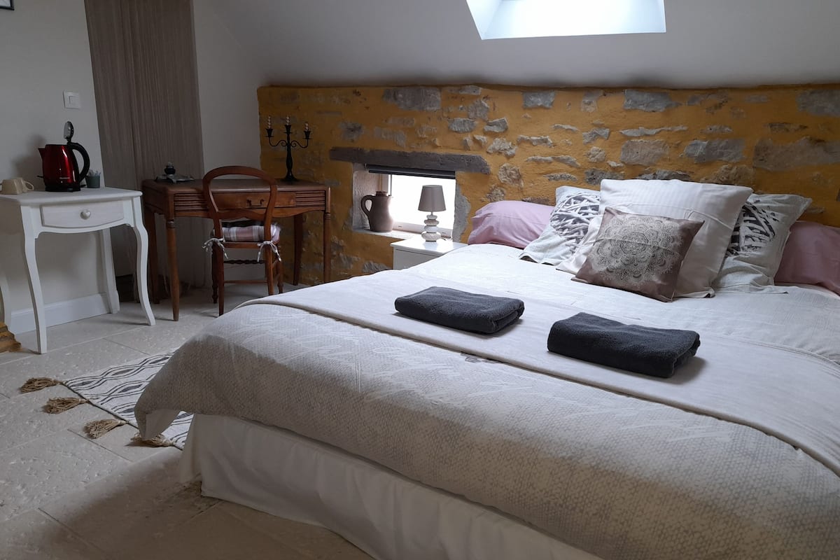 Ein Schlafzimmer mit einem Steinkopfteil, einem Bett mit zwei Handtüchern, einem Nachttisch, einem Stuhl und einem Schreibtisch mit Wasserkocher.