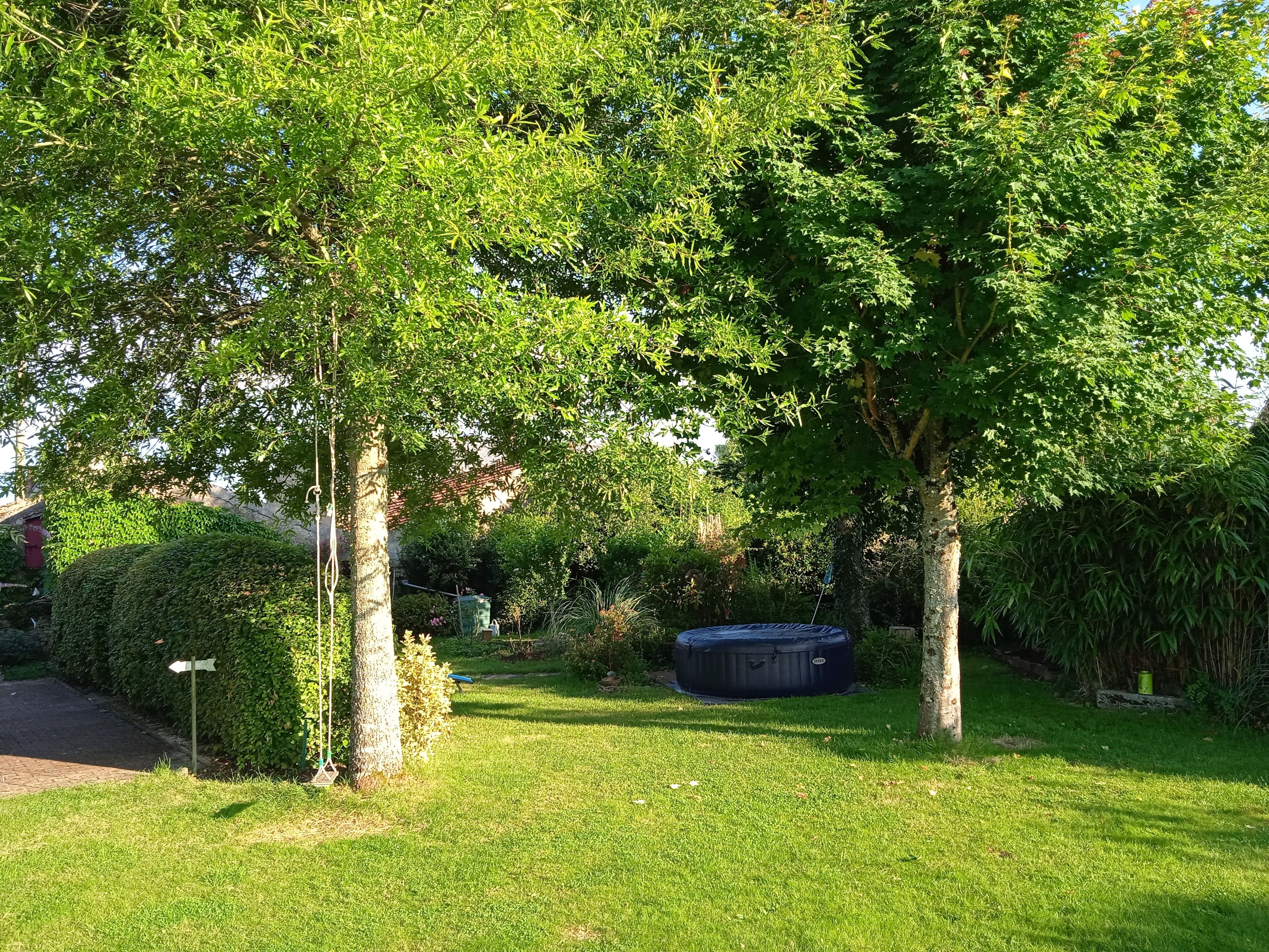 A well-maintained garden with mature trees, a neatly trimmed hedge, and a black outdoor heater.