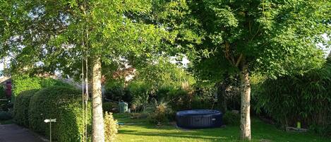 A well-maintained garden with mature trees, a neatly trimmed hedge, and a black outdoor heater.
