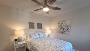 Une chambre à coucher comprenant un lit, deux tables de chevet, un ventilateur de plafond et des œuvres d’art murales.