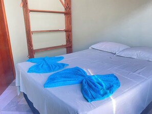 Comfortable bed with a tidy bedspread and two folded towels, set against a light-colored wall.