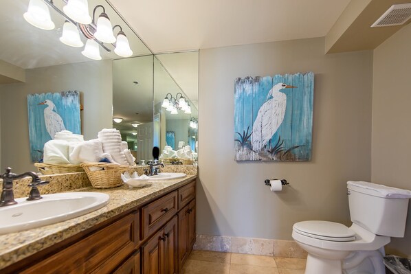A bathroom with a granite countertop, wooden cabinets, a white sink, a mirror, a toilet, and a painting of a bird on the wall. - ~3 BR 3 BA Updated unit All BR's on the Water @ The Long Beach, Tower 3~ (Panama City Beach)