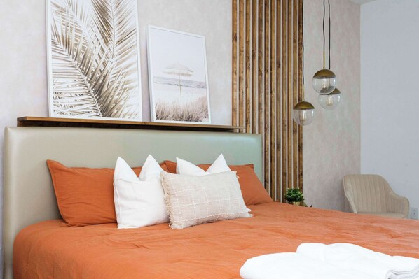 A neatly made bed with an orange bedspread and white pillows, a wooden headboard, and two framed pictures on the wall.