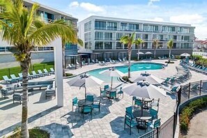 A modern hotel with a swimming pool, sun loungers, and outdoor seating areas.