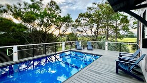 A swimming pool with a wooden deck, surrounded by trees and a view of a landscape. - Private Pool and Dock, Steps from the Beach, Beautiful Sunset Views (Saint Helena Island)