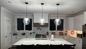 A modern kitchen with a large island, pendant lights, and a backsplash with a geometric pattern. - Private Pool and Dock, Steps from the Beach, Beautiful Sunset Views (Saint Helena Island)