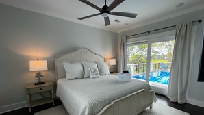 A bedroom with a large bed, a ceiling fan, a nightstand, a lamp, and a view of a swimming pool through a sliding glass door. - Private Pool and Dock, Steps from the Beach, Beautiful Sunset Views (Saint Helena Island)