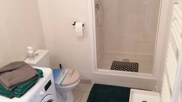 Ein kleines Badezimmer mit Waschmaschine, Toilette und Duschkabine.