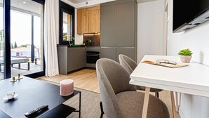 Een moderne keuken met houten kastjes, een eethoek met een tafel en stoelen, en een aan de muur bevestigde televisie.