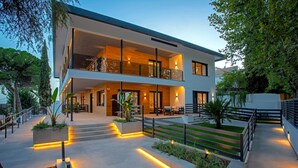 Een modern huis met twee verdiepingen, een balkon, buitenmeubilair en een verlicht pad.