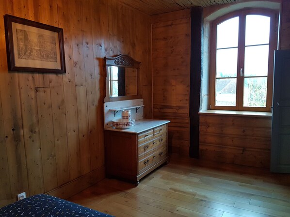 Une pièce en bois, avec une commode, un tableau encadré au mur et une fenêtre donnant sur un paysage.