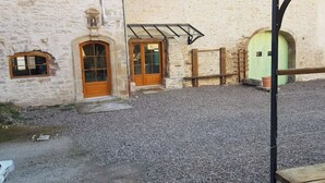 Ein Steinhaus mit zwei Holztüren und -fenstern, einer Schotterauffahrt und einer Metallkonstruktion.