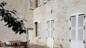 Ein Steinhaus mit weißen Fensterläden, einem Tisch und Stühlen in einer Außenbestuhlung.