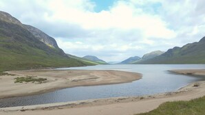 A natural landscape with a river, mountains, and a sandy beach.